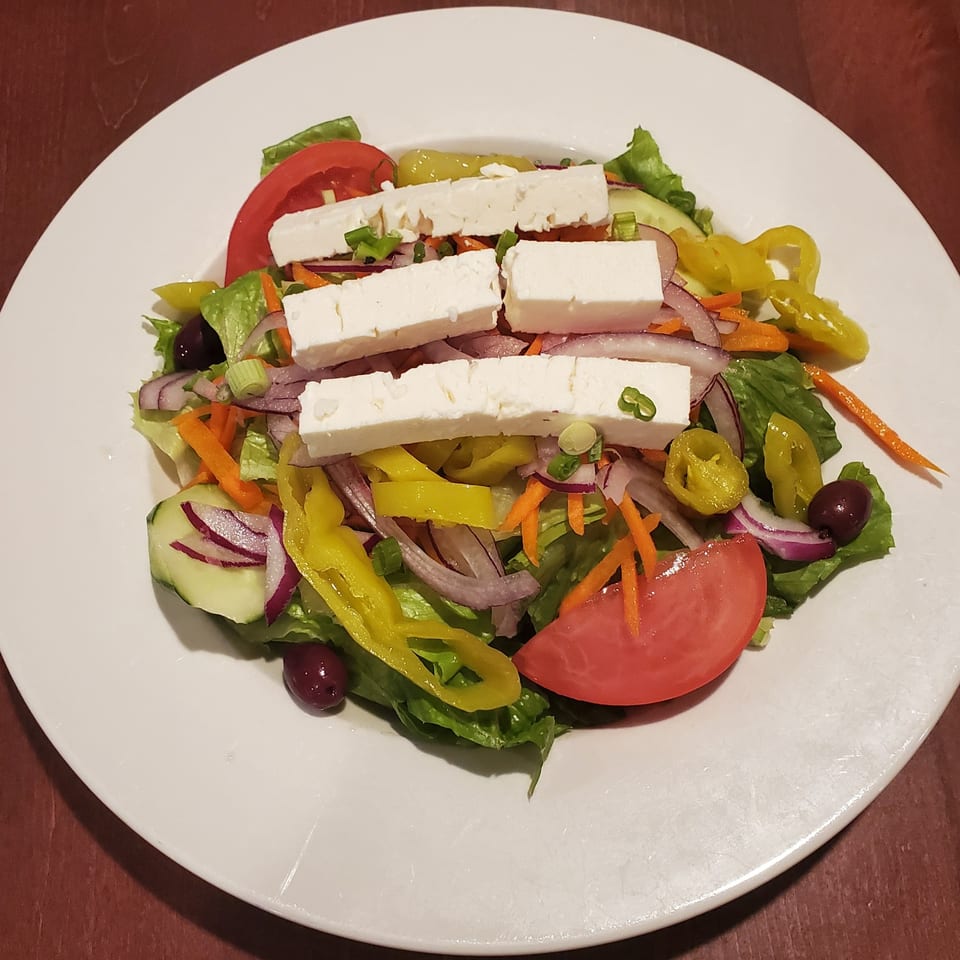 A fresh Greek salad with lettuce, tomatoes, cucumbers, red onions, olives, and feta cheese.