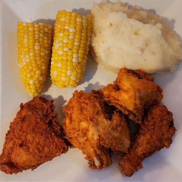 A plate of crispy fried chicken, two corn on the cob, and a scoop of mashed potatoes.