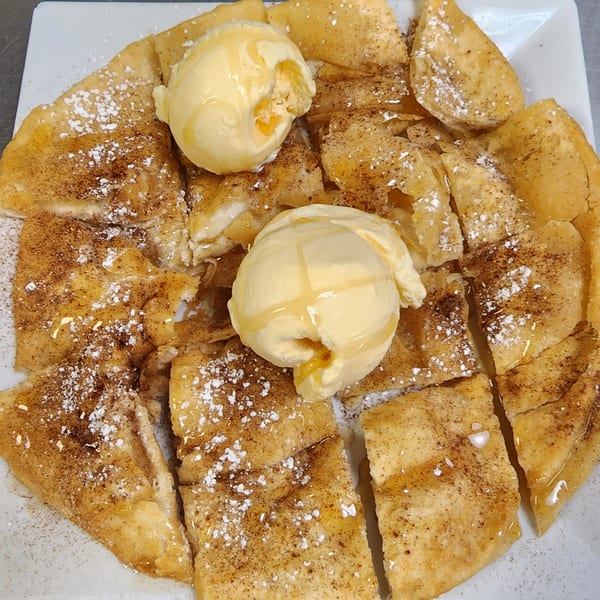 A plate of golden-brown dessert crepes, cut into triangles, topped with two scoops of vanilla ice cream, honey, cinnamon, and powdered sugar.