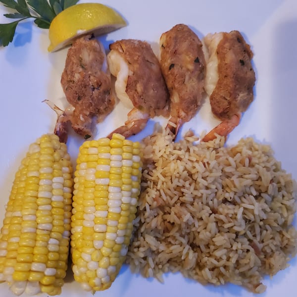 Stuffed shrimp with rice pilaf and two corn on the cob, garnished with lemon and parsley.