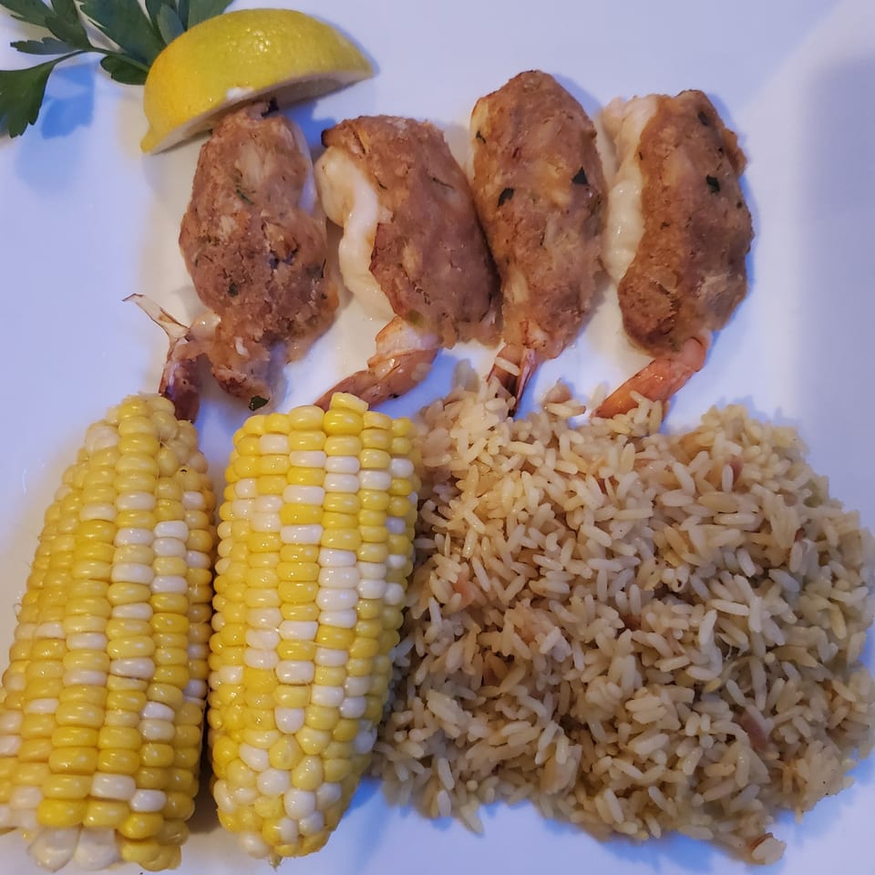Stuffed shrimp with rice pilaf and two corn on the cob, garnished with lemon and parsley.