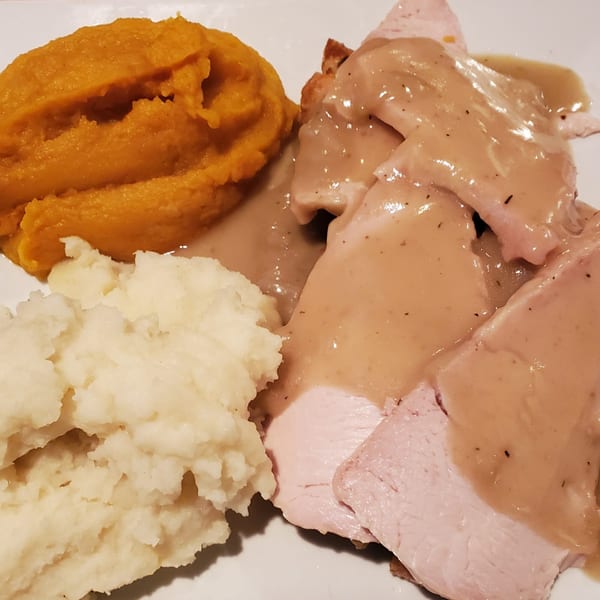 Sliced turkey with gravy, mashed potatoes, and mashed sweet potatoes on a white plate.