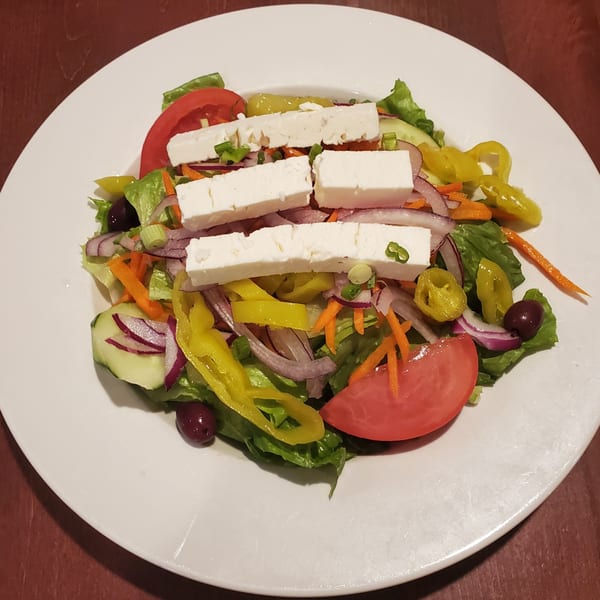 A fresh Greek salad with feta cheese, tomatoes, olives, onions, and peppers on a white plate.