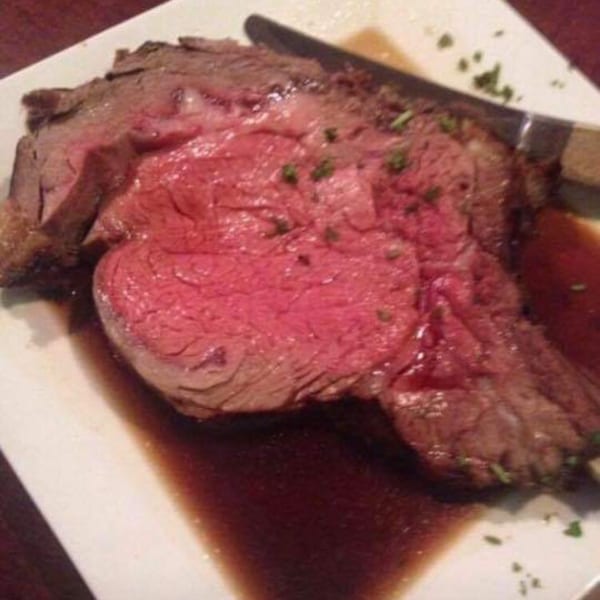 A thick slice of rare prime rib with gravy and a knife on a white plate.