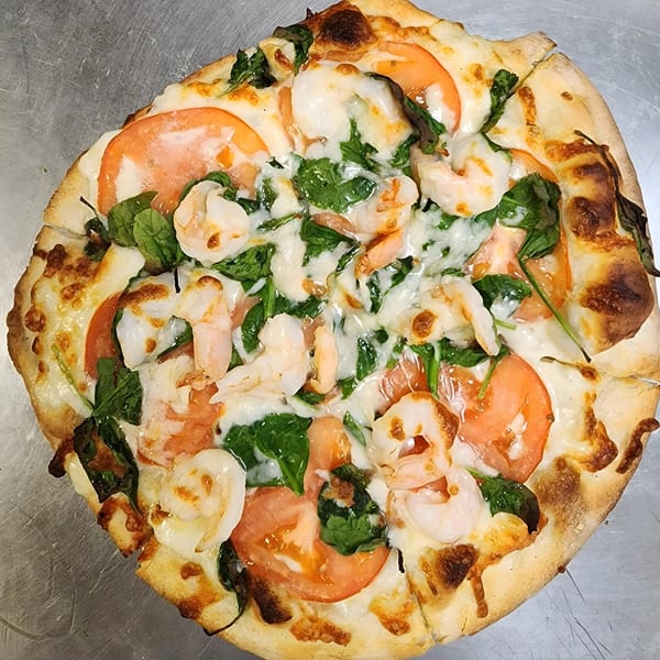 A Wardhurst Restaurant shrimp pizza with tomatoes, spinach, and melted cheese on a metal surface.
